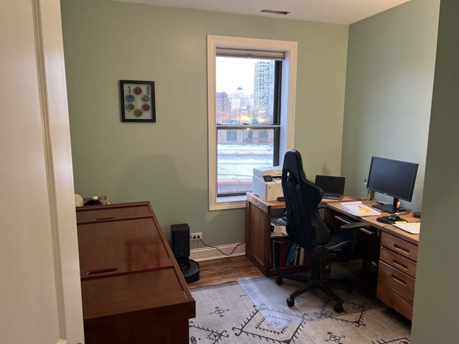 Home office with desk, computer, printer, and chair; green walls, wooden desk, and rug.