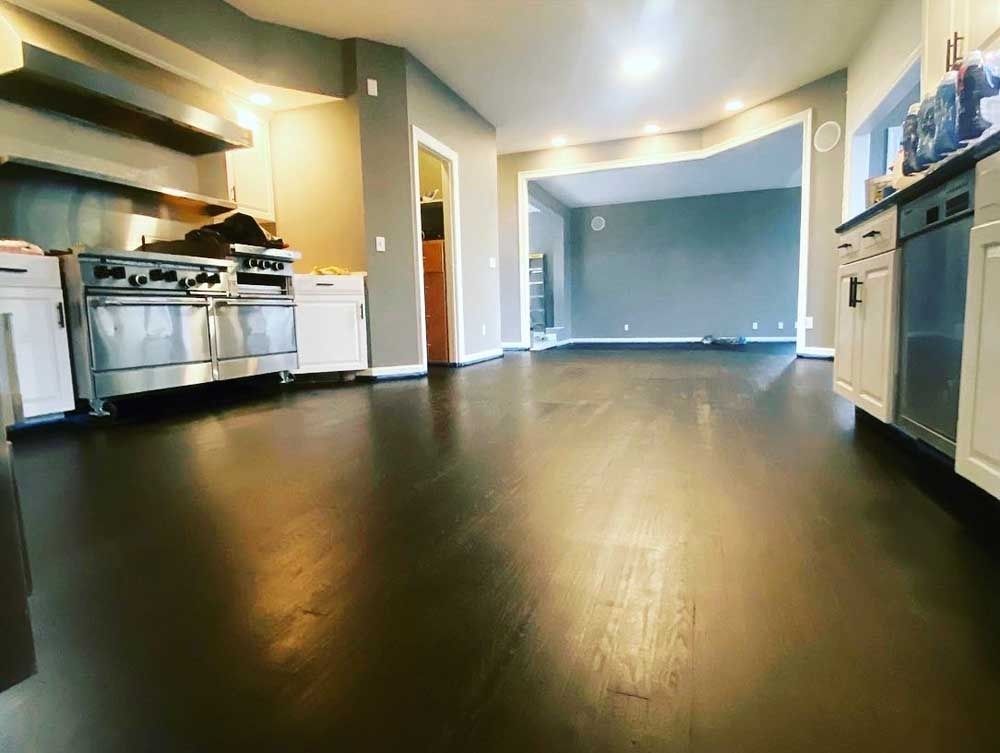 Dark wood floors in a kitchen, stainless steel appliances, and a gray-walled living room visible in the background.
