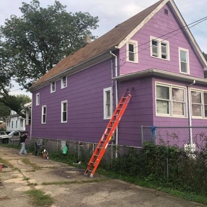 A purple house with a brown roof and a tall orange ladder propped against it.