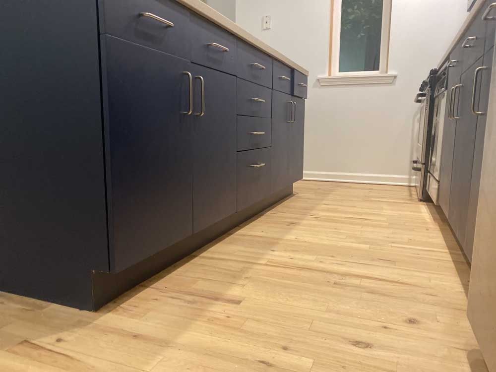 Low angle shot of blue kitchen cabinets with silver hardware and light wood floors.
