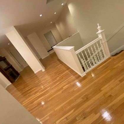 Hardwood floors in a house. Staircase with white railing and walls. Dim lighting.