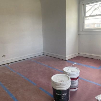 Empty room with pink floor covering and paint cans. White walls, window, and baseboards.