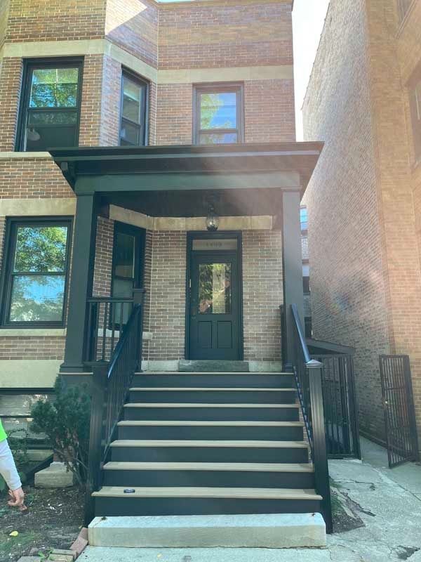 Brick building entrance with black stairs, railings, and porch. Black door and window frames.