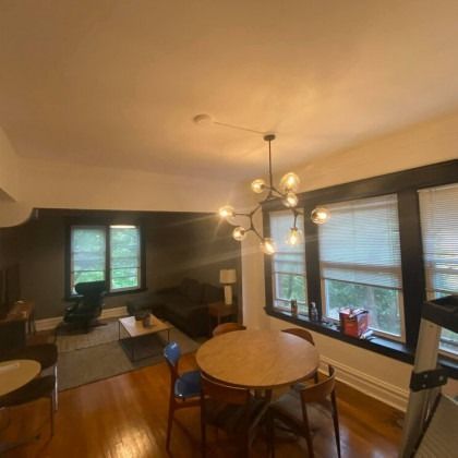 Living room with wood floors, round table, chandelier, and multiple windows with blinds.