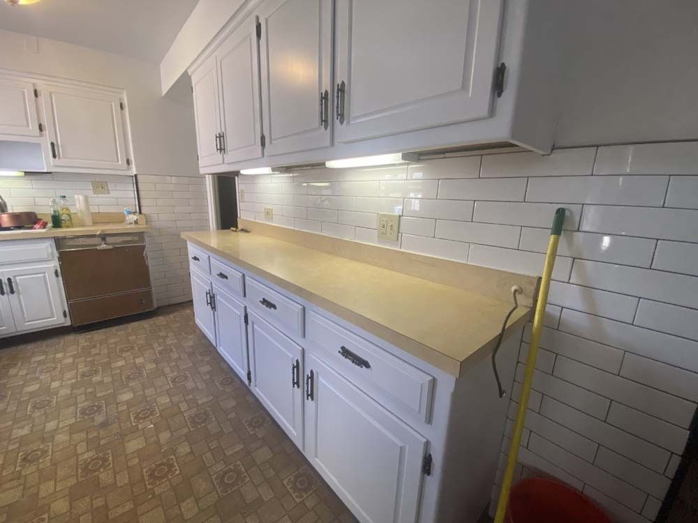 White kitchen cabinets, beige countertops, white subway tile backsplash, and linoleum floor.