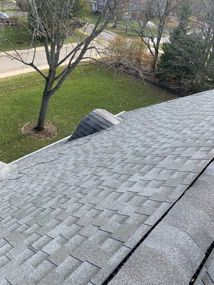 Gray asphalt shingle roof with a small dormer. Green grass and trees in the background.