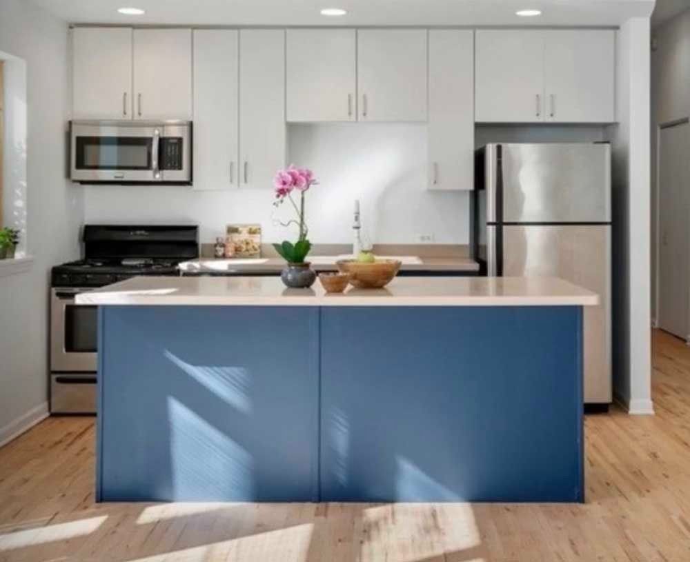 Blue and white kitchen with island, stainless steel appliances, and wooden floor.