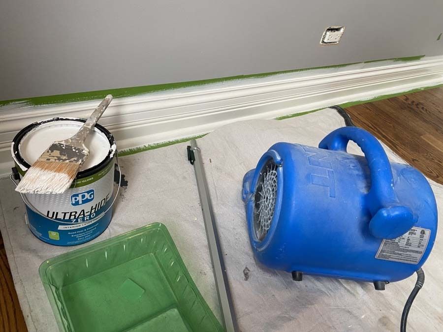 Paint supplies: open paint can, brush, tray, and a blue blower on a drop cloth.