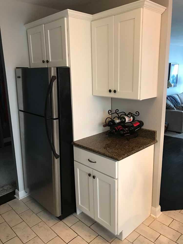 White kitchen cabinets, refrigerator, and countertop with a wine rack.