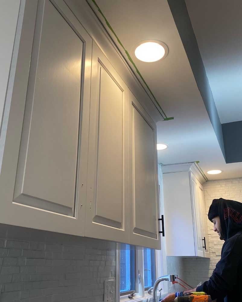 White kitchen cabinets with black handles. A person is working in the kitchen.