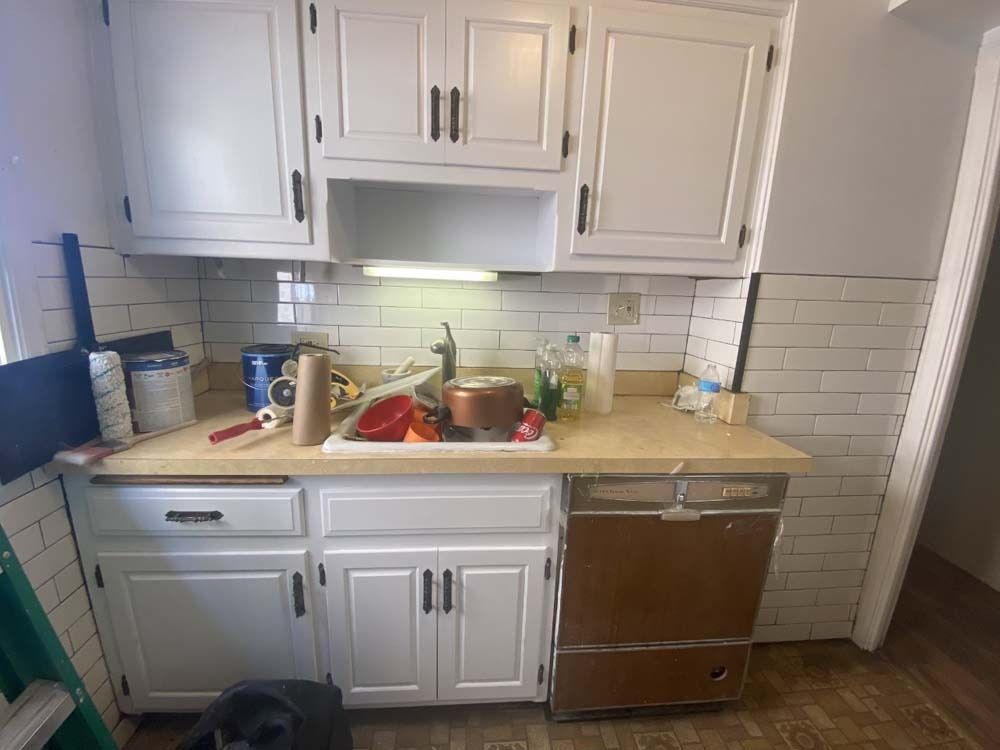 Kitchen with white cabinets, beige countertop, and brown dishwasher during renovation.