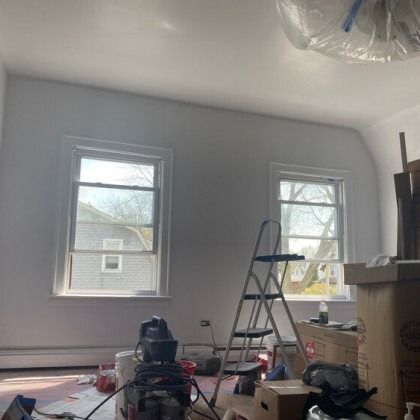 Room with two windows, a ladder, and painting supplies, during renovation.