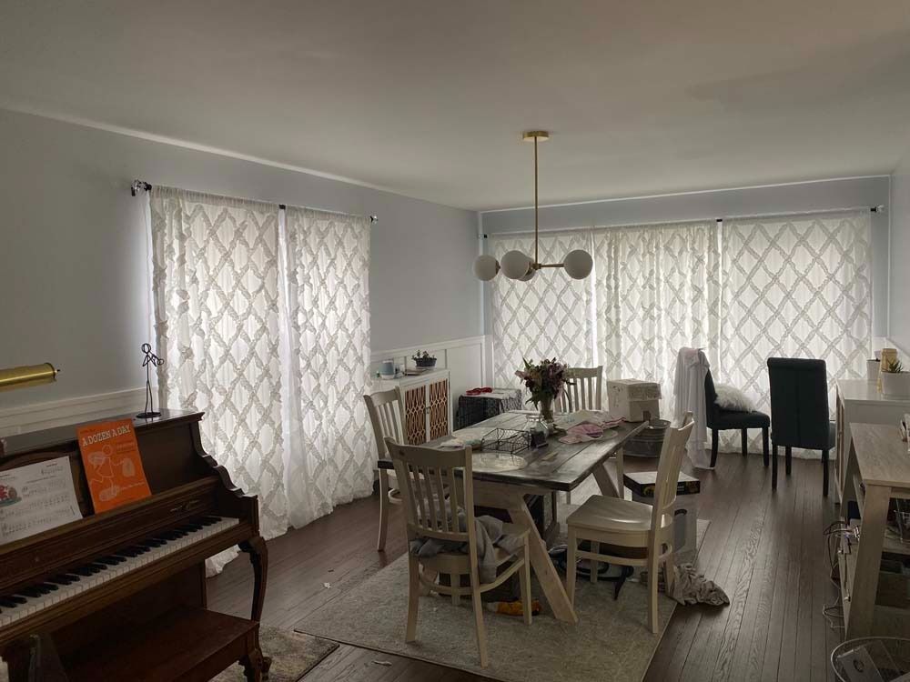 Living room with piano, dining table, and patterned white curtains.