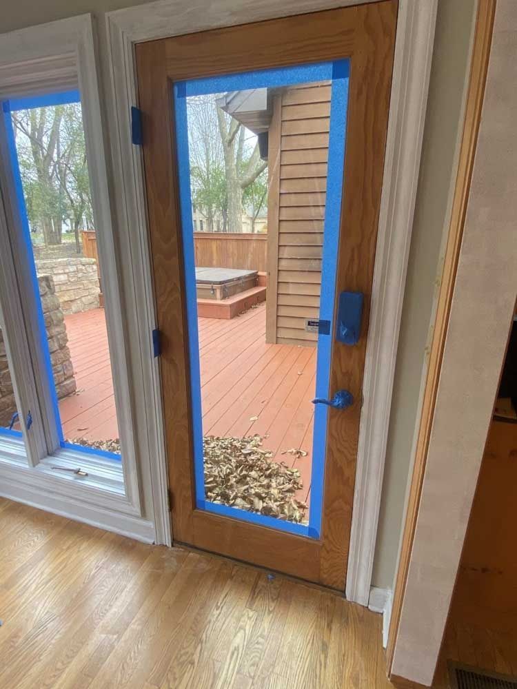 Door and window frames with blue painter's tape, leading to a wooden deck.