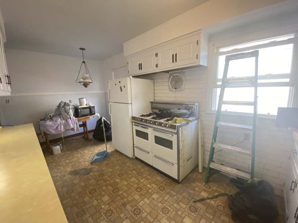 Kitchen with white cabinets, refrigerator, vintage stove, and ladder near window.