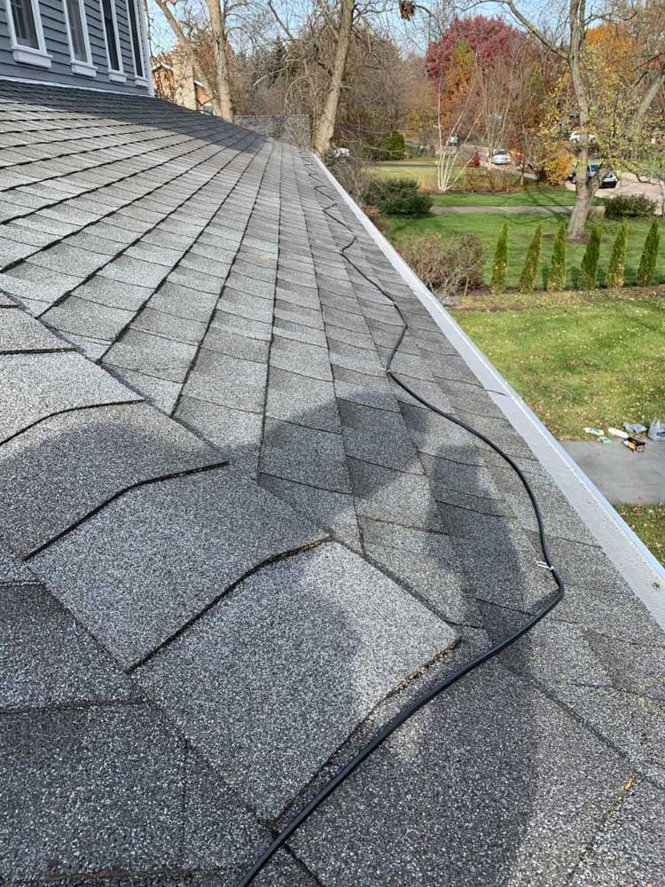 Gray asphalt shingle roof with a gutter, viewed from above, with a green yard in the background.