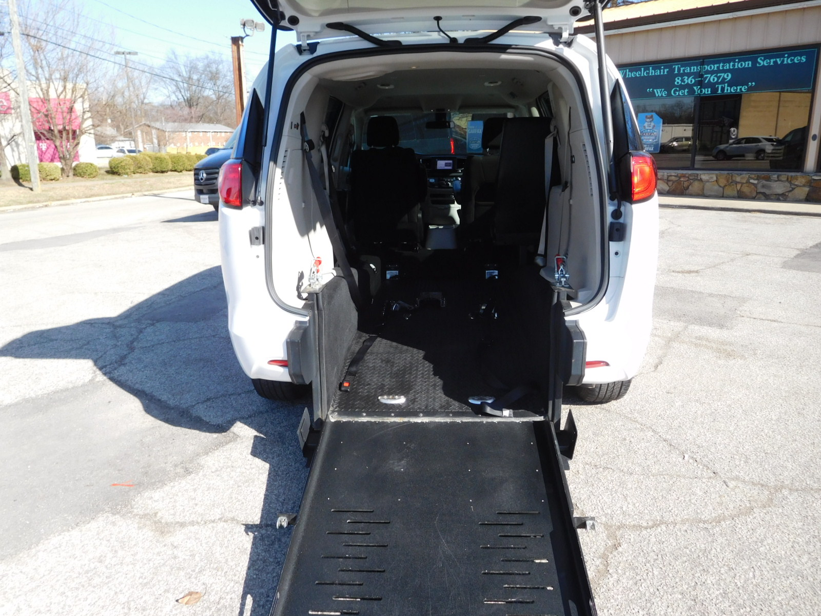 Man in wheelchair on a lift entering accessible van. Yellow handrails, blue sky, sunlight.
