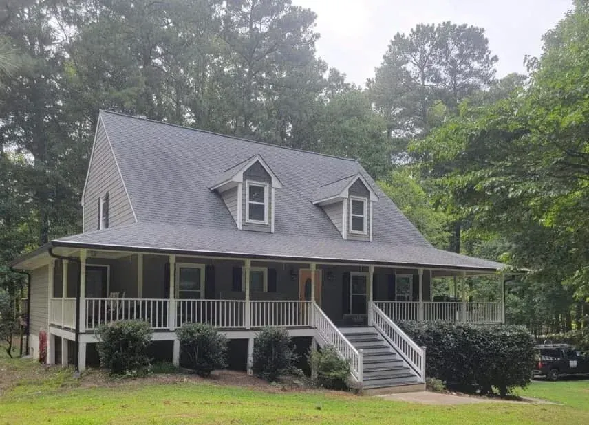A high-angle view of a roof valley with gray shingles, white gutters, and a white downspout mounted on a brick wall.