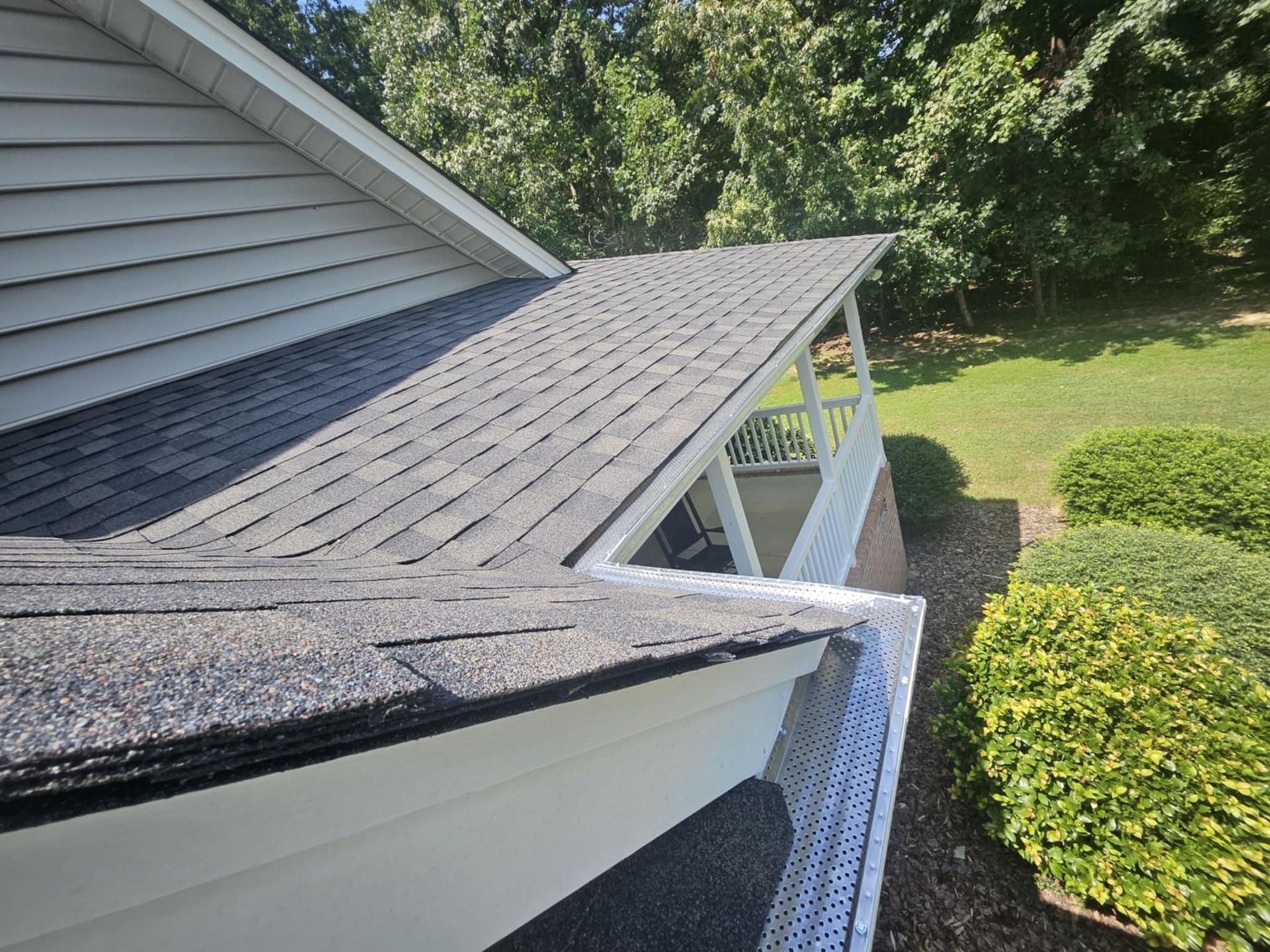 A mesh gutter guard installed on a residential roof edge, with trees and a garden in the background.