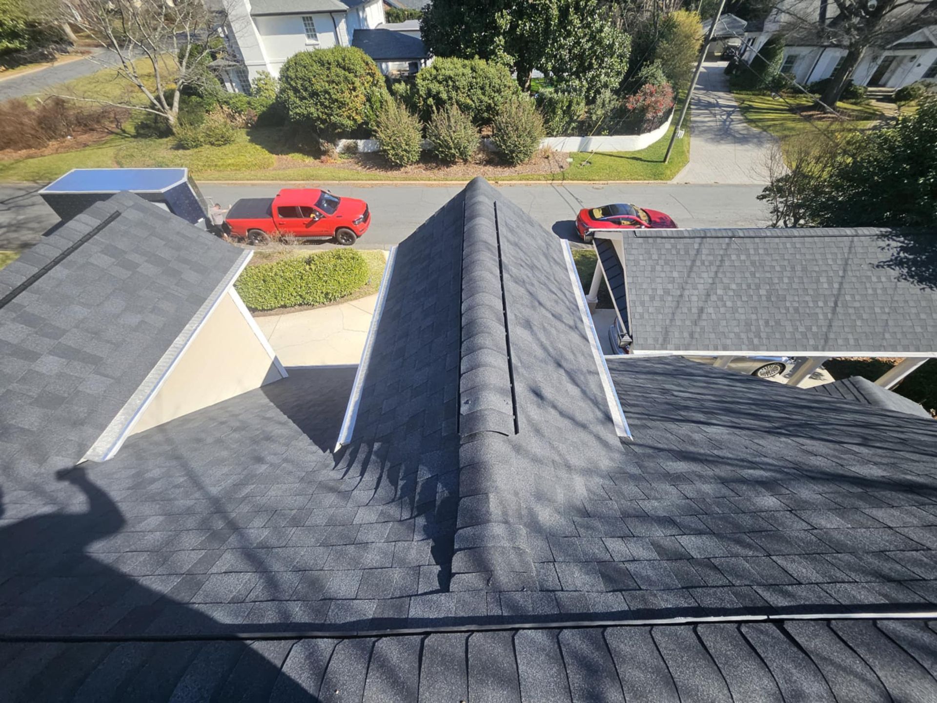 An elevated view along the edge of a shingled roof and metal gutter, looking out over a yard with a trailer and trees.