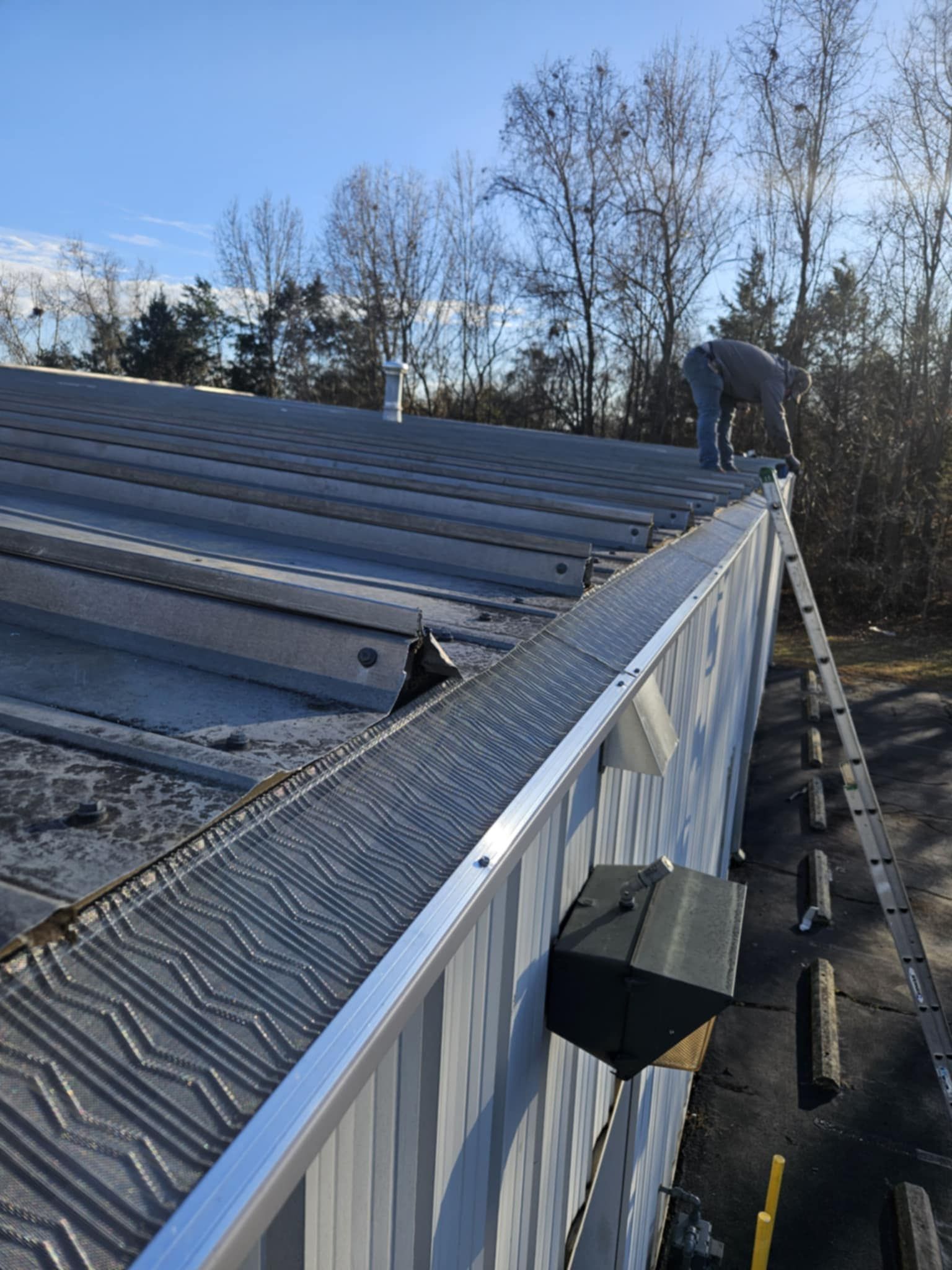 A white downspout connected to gutters against a red brick house wall, leading into a drainage pipe in the concrete patio.