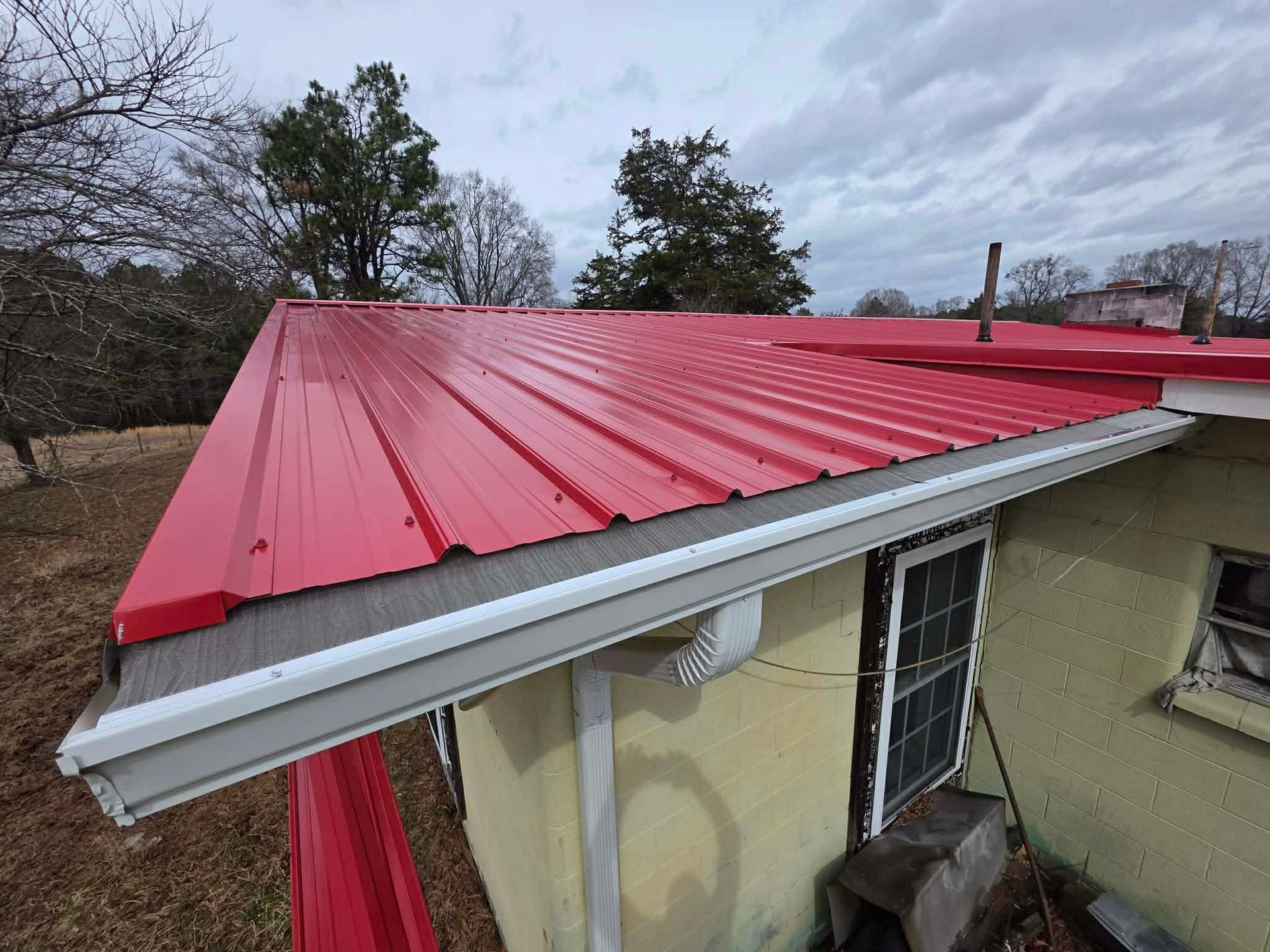 A red corrugated metal roof with white gutters on a house exterior under a cloudy sky.