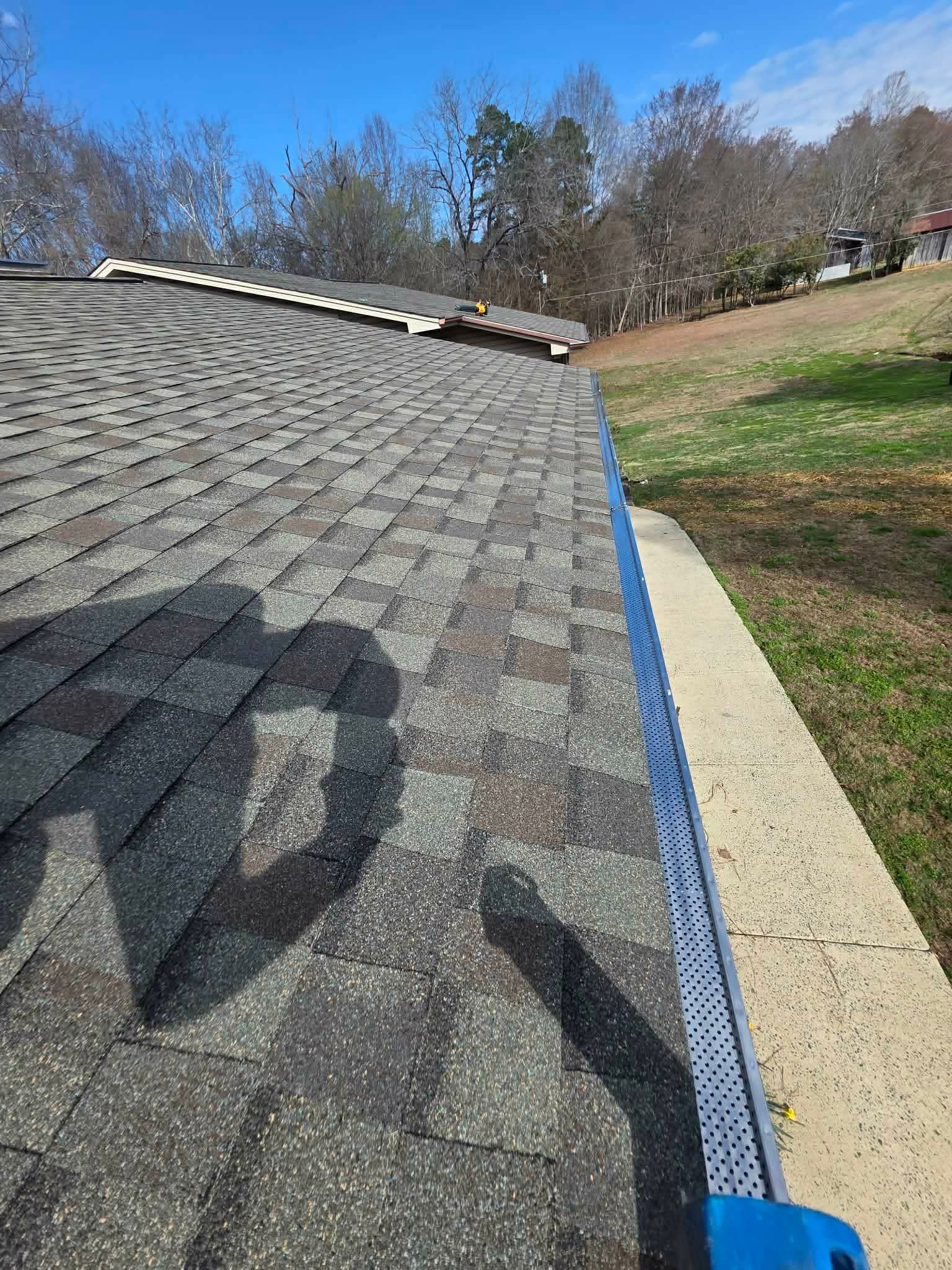 A grey shingled roof with a dark shadow cast across the surface, leading to a mesh gutter guard along the edge.