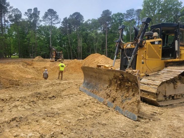 Bulldozer at a dirt construction site with workers and piles of sand under a cloudy sky