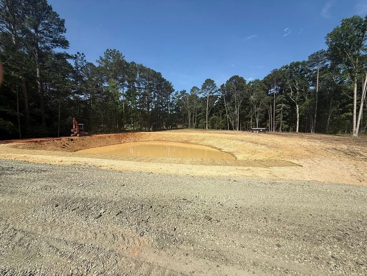 Cleared dirt lot with graded earth and trees lining the background under a blue sky