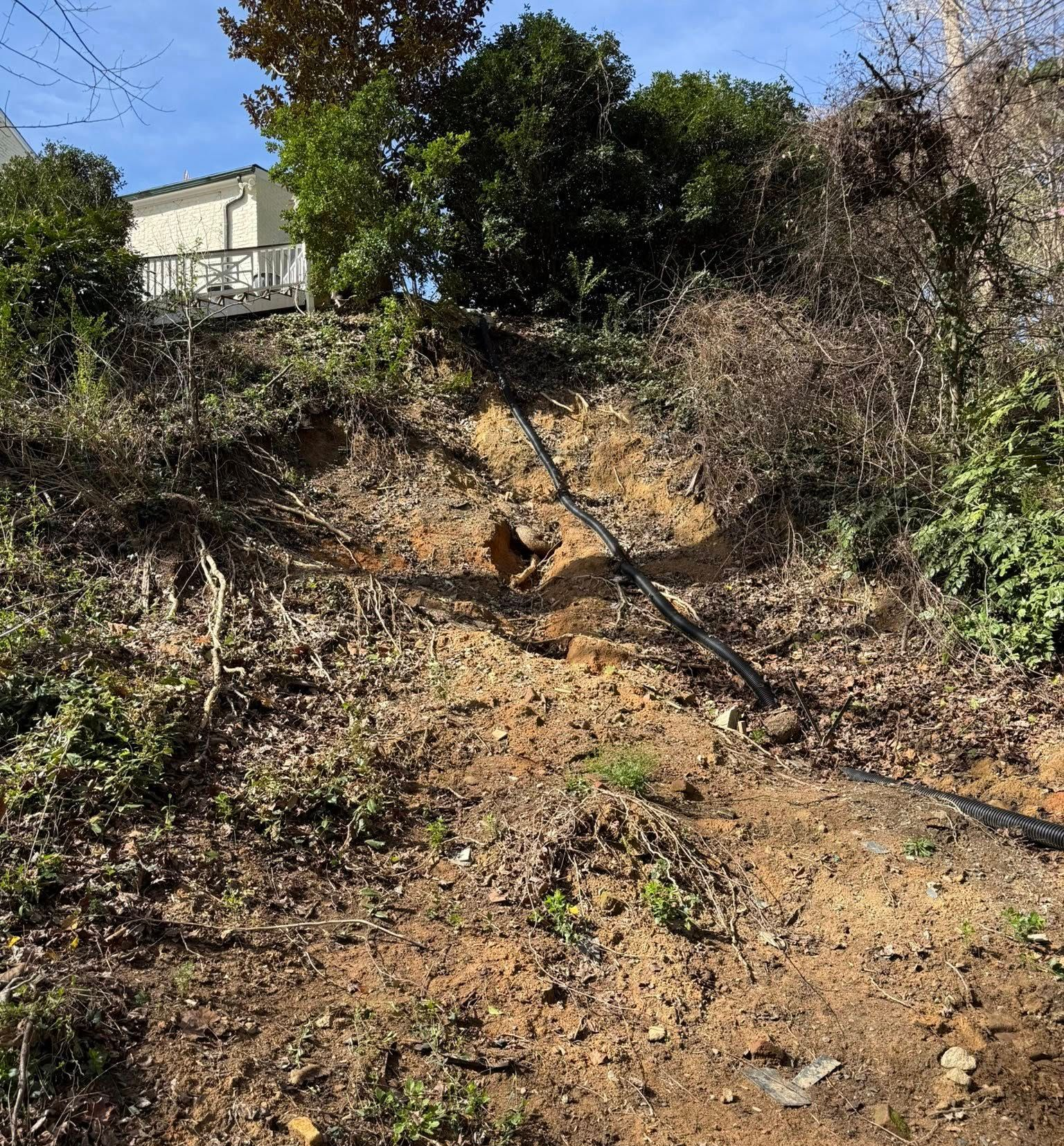 Steep dirt hillside with scattered brush and a small white structure at the top left.