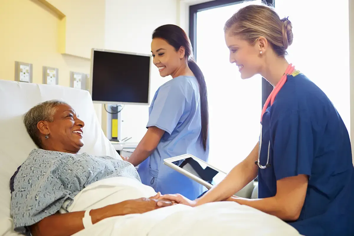 A nurse is talking to a patient in a hospital bed.