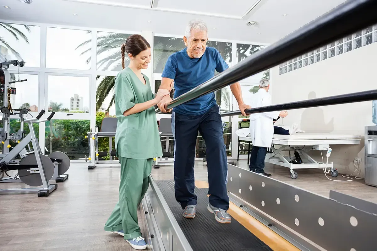 A nurse is helping an elderly man walk on a treadmill.