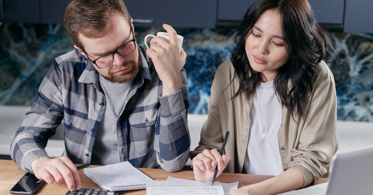 A man and a woman are sitting at a table looking at papers and a laptop.