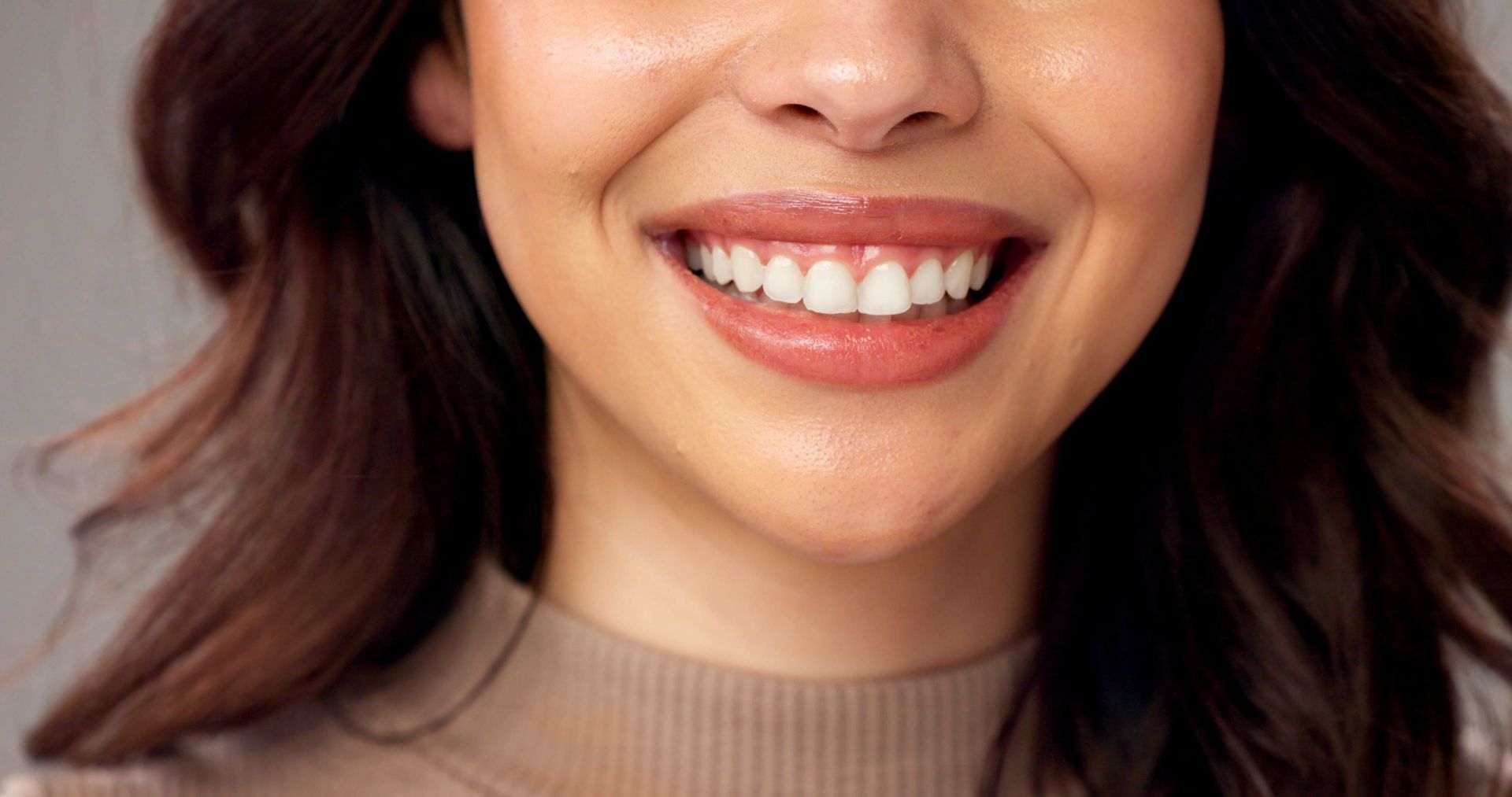 Close-up of a smiling mouth with bright white teeth and glossy, nude-colored lips.