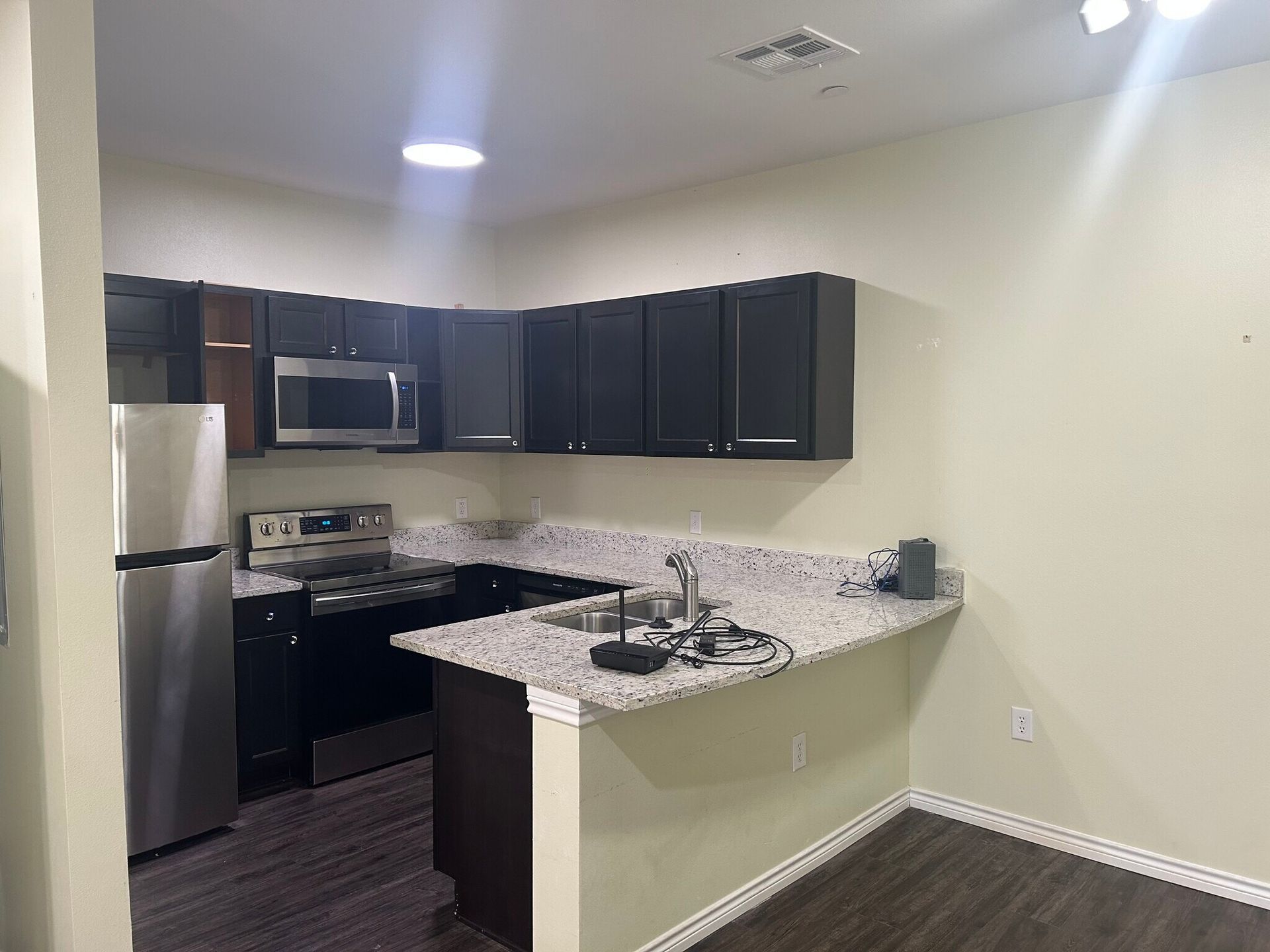 A kitchen with black cabinets , stainless steel appliances , granite counter tops and a refrigerator.