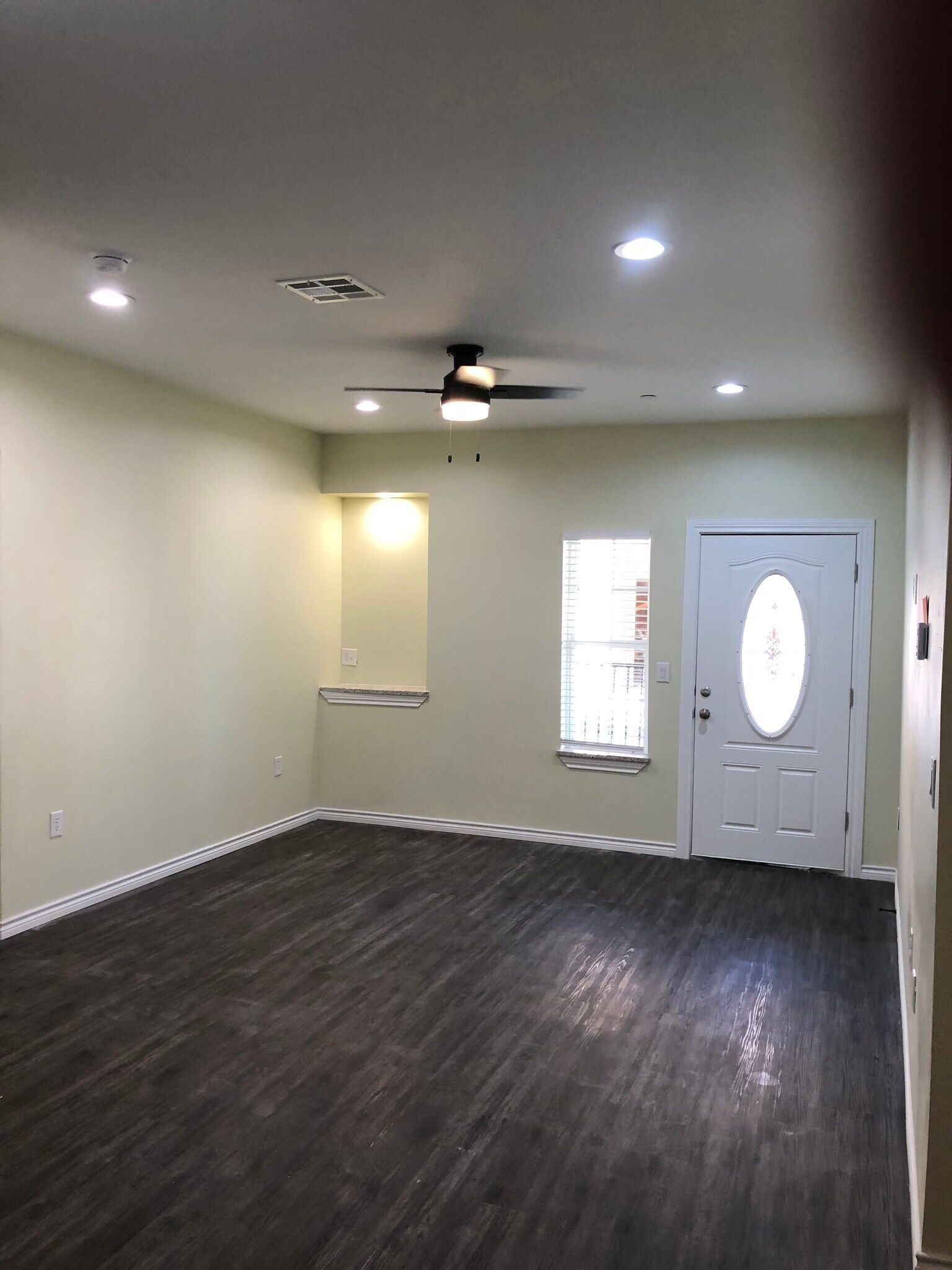 An empty living room with a ceiling fan and a door.