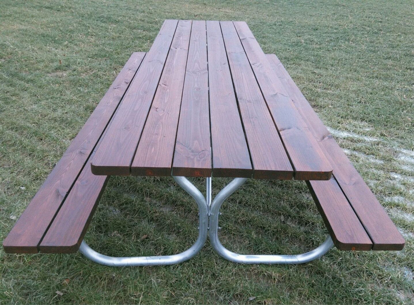 Picnic table with brown wooden top and silver metal legs, set on grass.