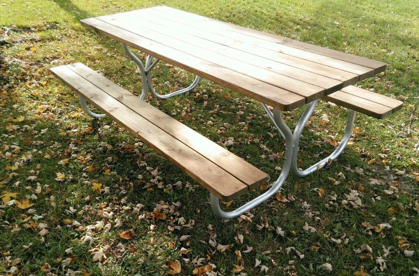 Picnic table with light brown wooden planks and silver legs, in grassy area.