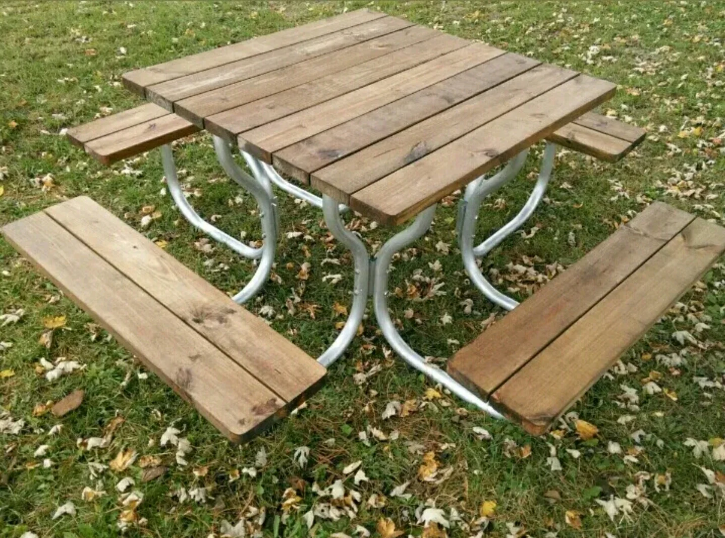 Square wooden picnic table with attached benches on a grassy lawn.