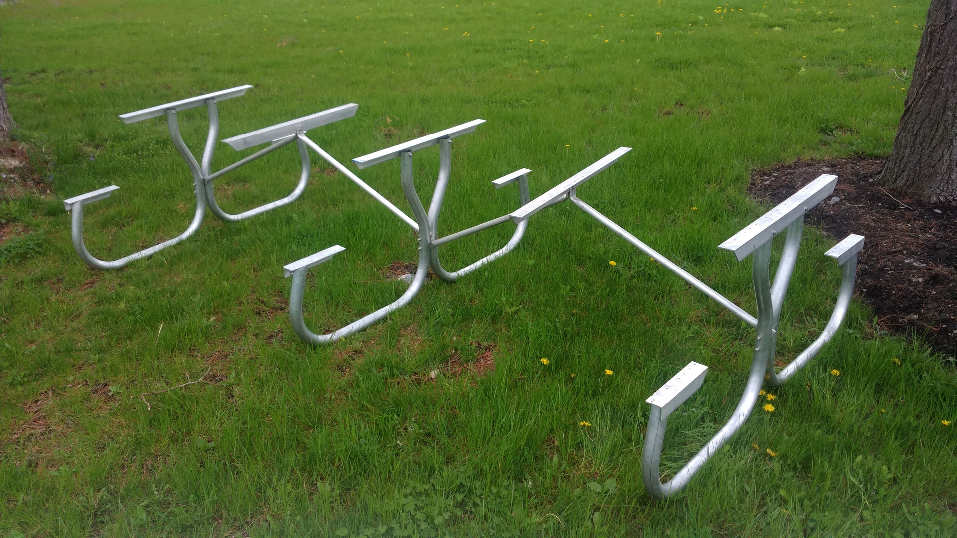 Three silver metal picnic table frames on green grass.