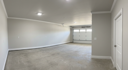 Empty beige garage with concrete floor and closed white door, viewed from the interior.