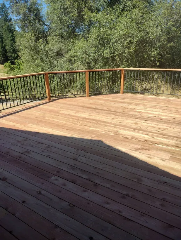 An empty wooden deck with a metal railing and trees in the background.