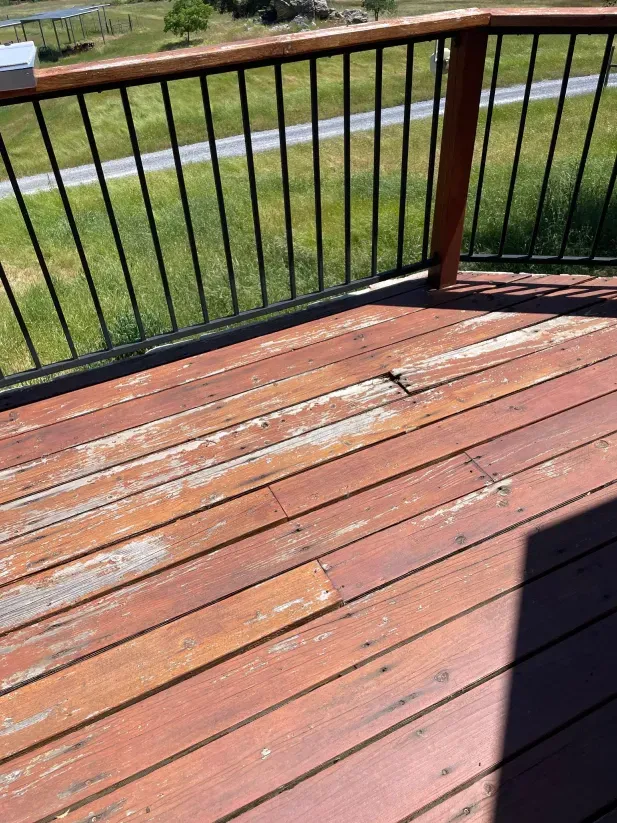 A wooden deck with a metal railing and a view of a field.