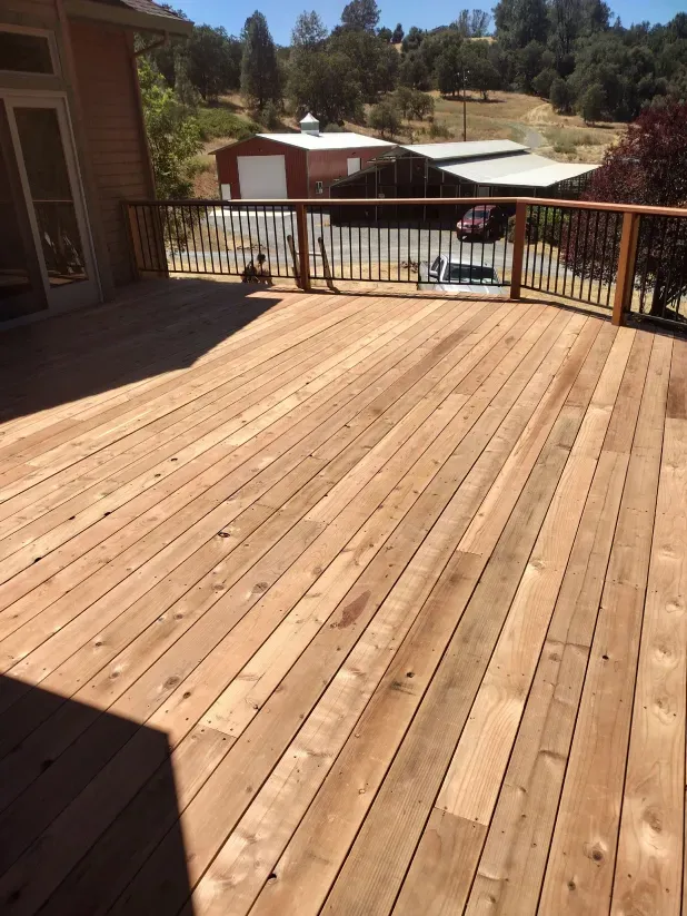 A large wooden deck with a railing and a house in the background