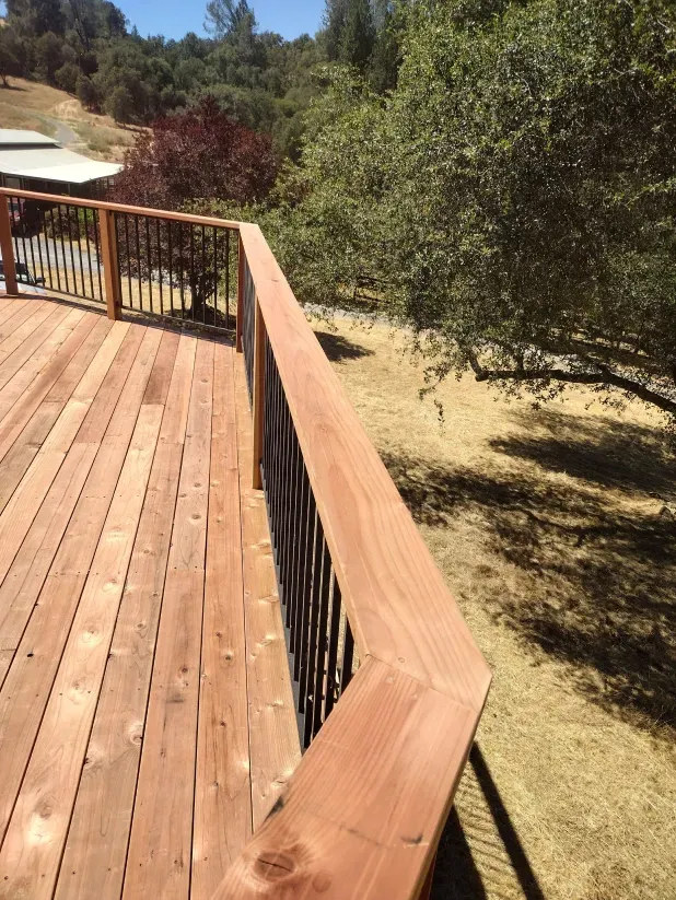 A wooden deck with a metal railing and trees in the background