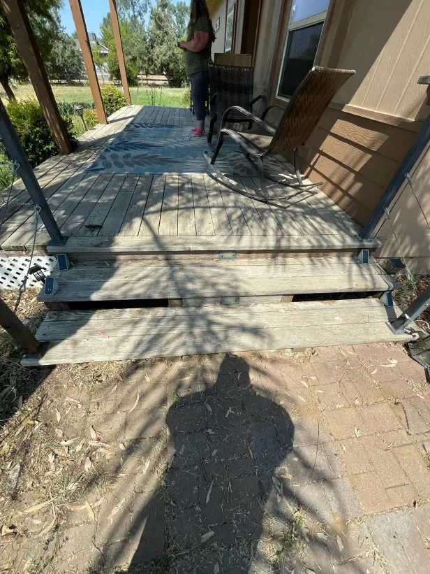 A person is standing on a wooden porch next to a rocking chair.