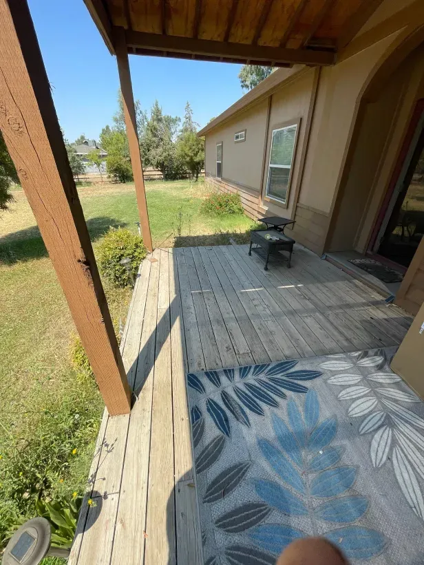 A person is sitting on a porch with a rug on it.