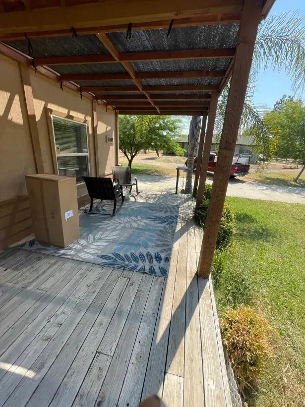 A wooden porch with a metal roof and a rug on it.