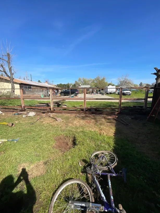 A bicycle is parked in the grass in front of a wooden fence.
