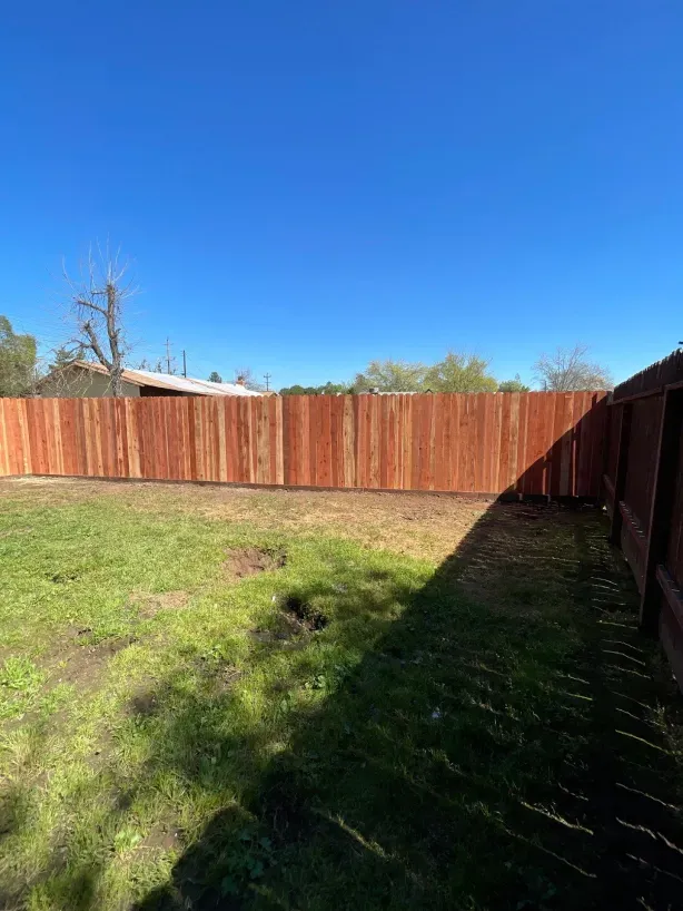 A wooden fence is in the middle of a grassy yard.